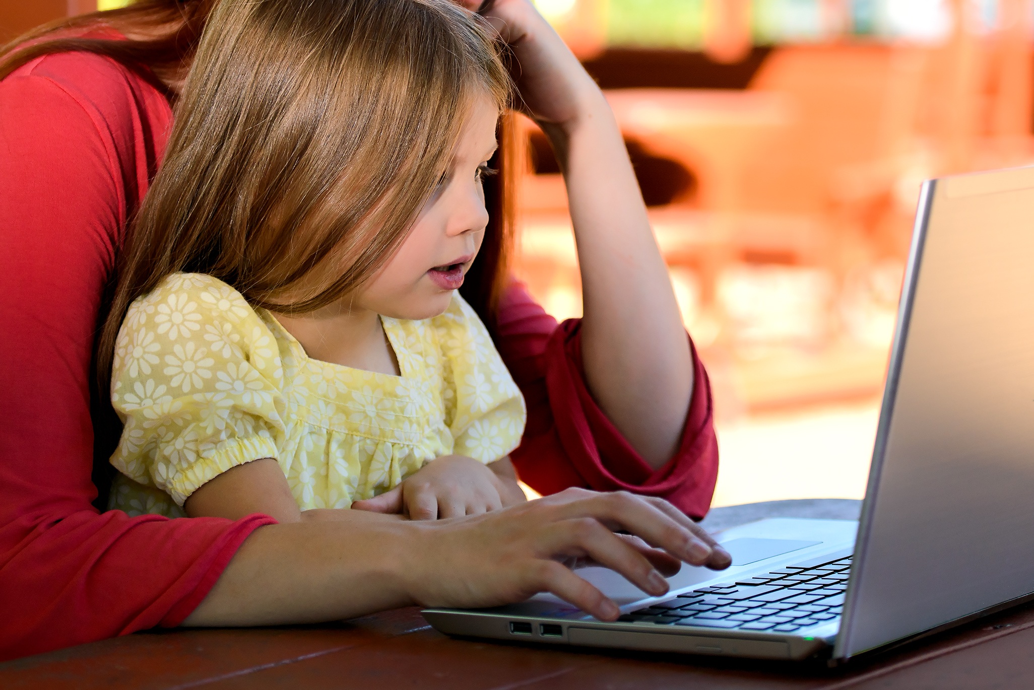 Mãe e filha sentada diante da tela de um computador navegando na internet